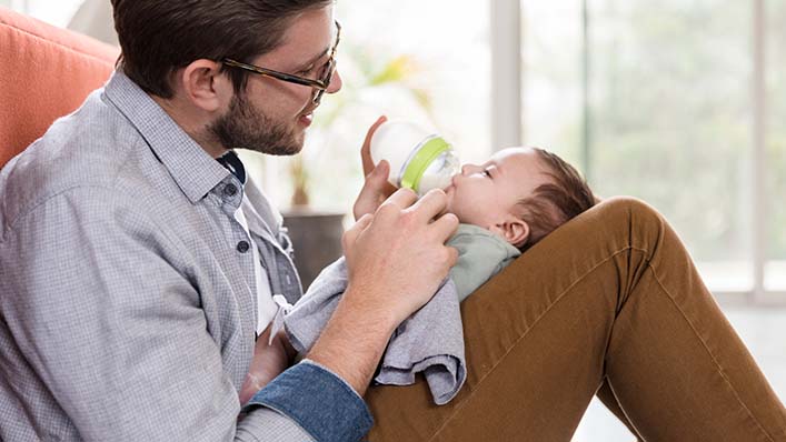 A father bottle feeds a baby in his lap.