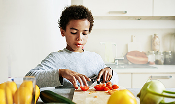 image: a boy in the kitchen cutting up tomatoes for a salad