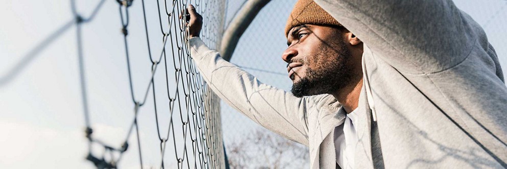 A man braces himself against a chain link fence and looks through the gaps.