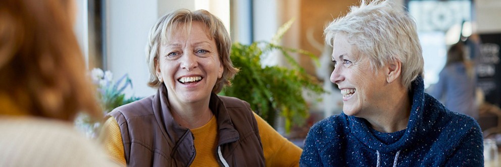 Three middle-aged women laugh as they talk and have coffee together.