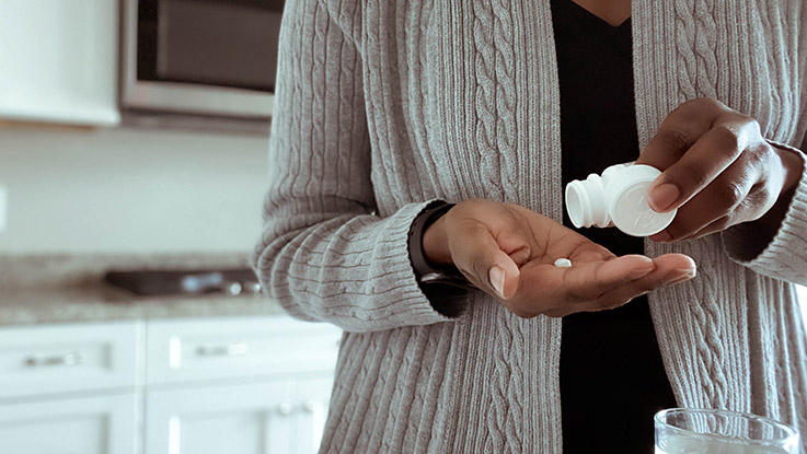 A woman shakes a melatonin pill out of a bottle of melatonin into her palm to take before bedtime.