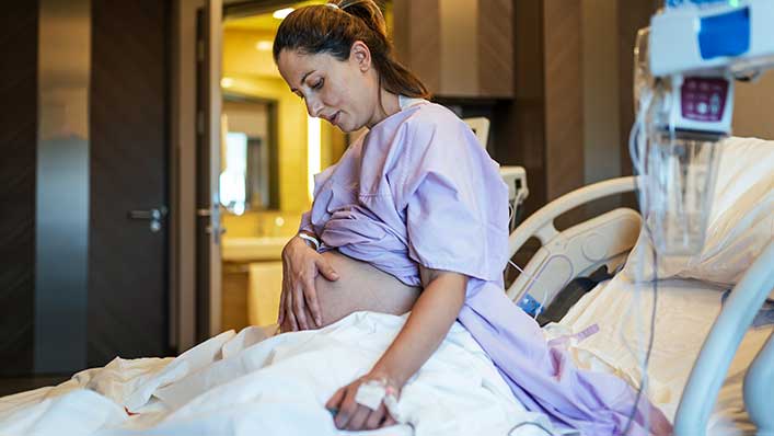 pregnant woman sitting up in a hospital bed, holding her belly.