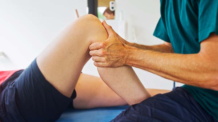 A physiotherapist guides an arthritis patient through knee mobility exercises.