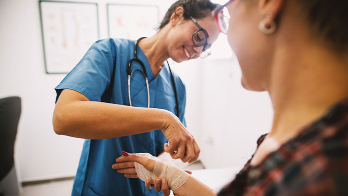 A smiling nurse wraps a patient's wrist in an elastic bandage.