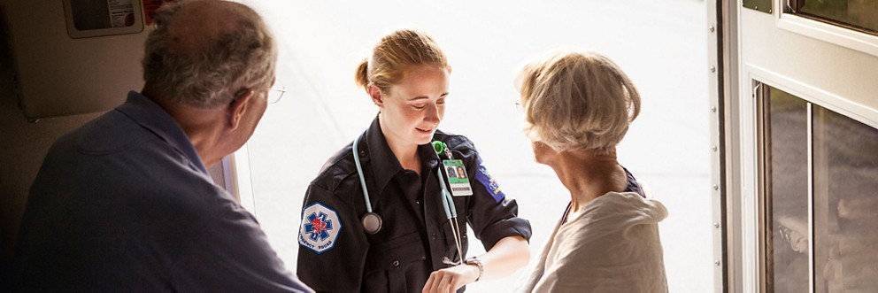A paramedic uses her watch to track an elderly woman's pulse in the back of an ambulance.