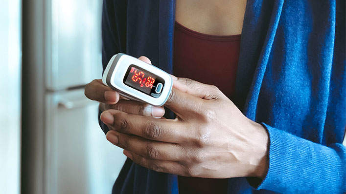 A woman wears a pulse oximeter on her finger at home.