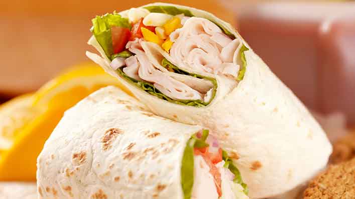 A tortilla wrap cut in half to reveal the ingredients inside, including meat, spinach, and slices of bell pepper.