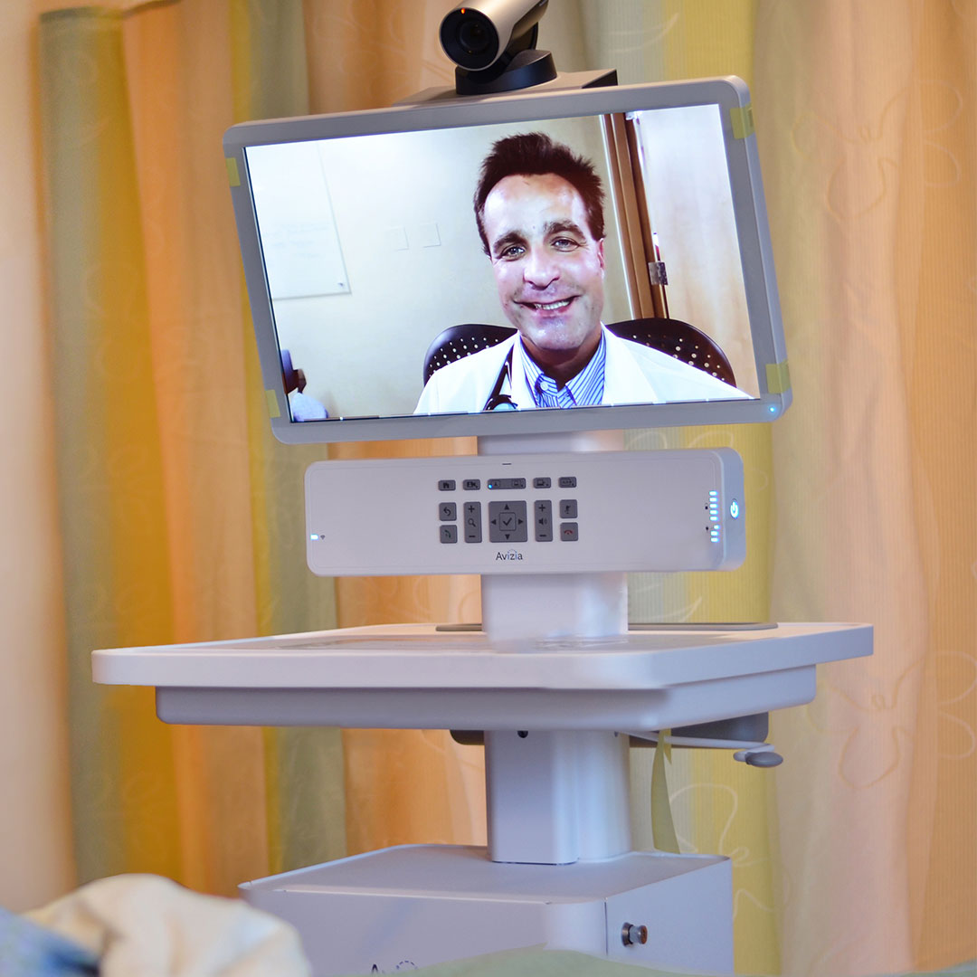 A doctor is video streamed into a patient room through a telemedicine cart.