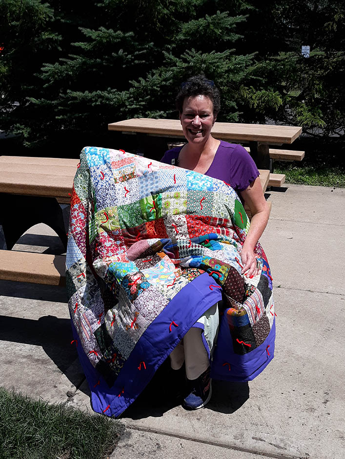A smiling woman holds up the quilt she made. 