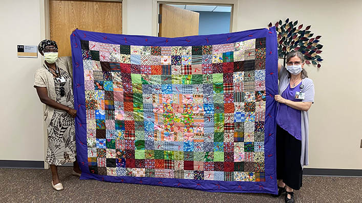 Two HealthPartners employees hold up a beautiful quilt.