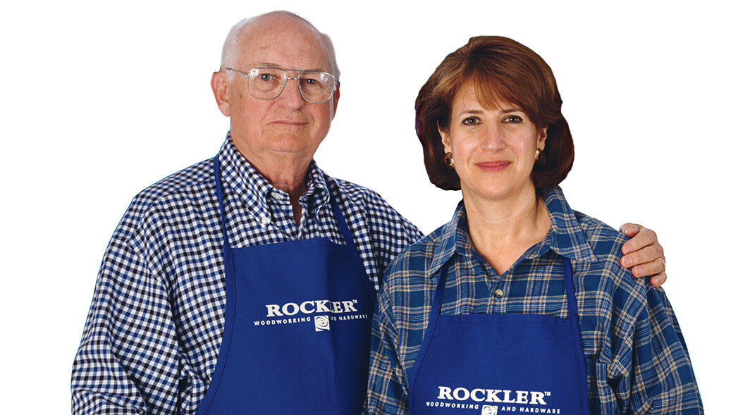 An older man and woman pose for a photo wearing Rockler work aprons.