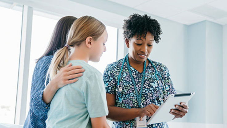 Mother and daughter talking to a healthcare professional with a clipboard.