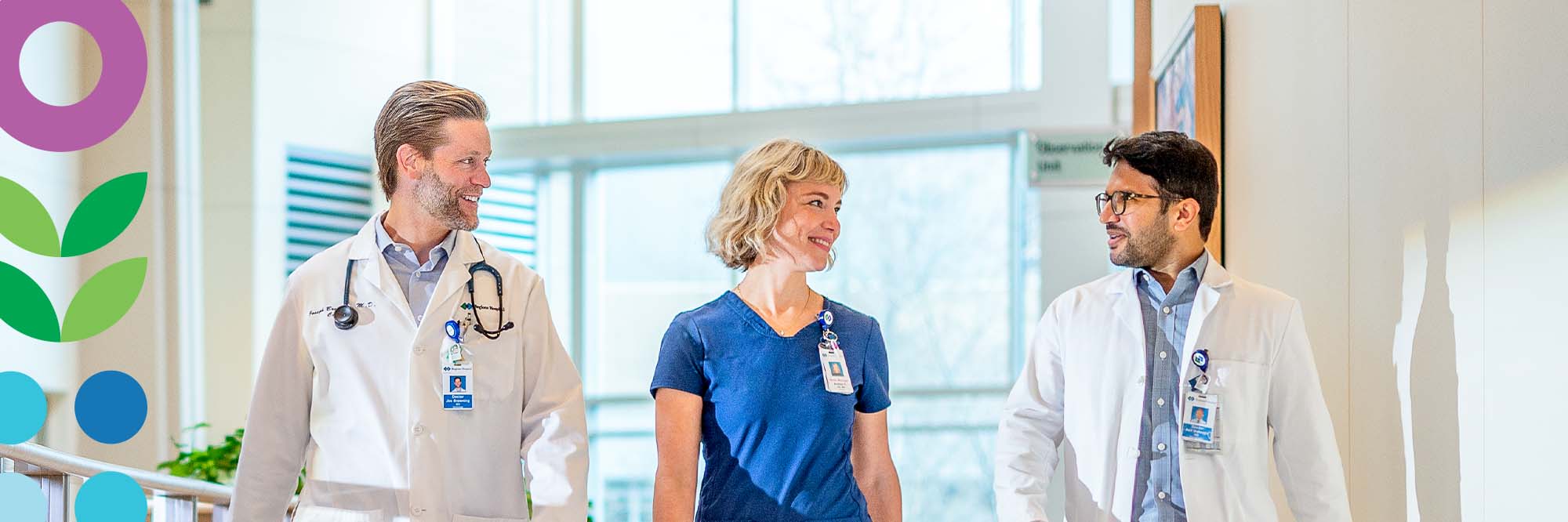 Three doctors chat while walking down a brightly lit hallway together.