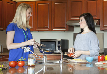 A young woman cooks with a dietitian in a kitchen at Melrose Center.