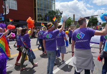 HealthPartners employees wearing HealthPartners shirts walk in the Pride Parade waving rainbow flags and gear.