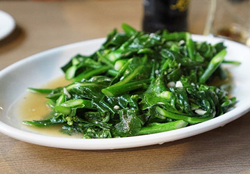 A white plate with a heaping serving of sauteed bok choy.