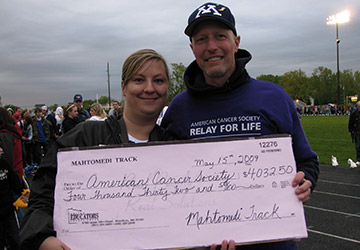 Two people hold an oversized check made out to the American Cancer Society