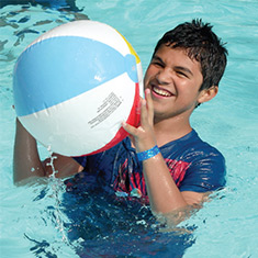 A smiling boy catches a beach ball in the pool.
