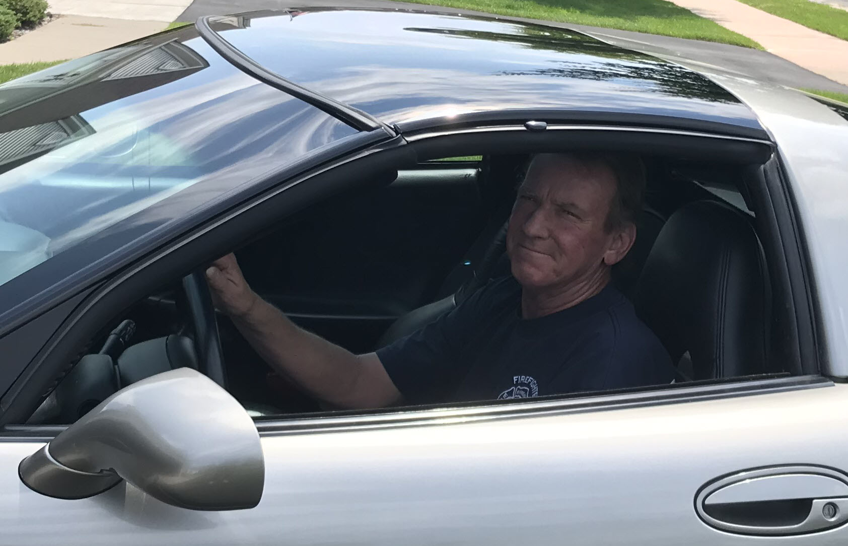 Mark Raeker sits in the driver's seat of a silver sedan in his driveway.